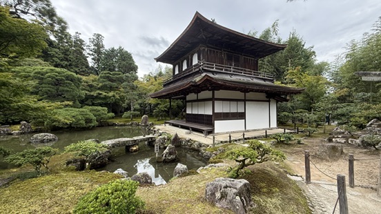 銀閣寺觀音殿深色木造二層建築，白牆黑瓦，周圍是水池與松樹