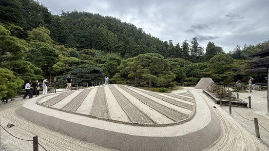 銀閣寺觀音殿深色木造二層建築，白牆黑瓦，周圍是水池與松樹