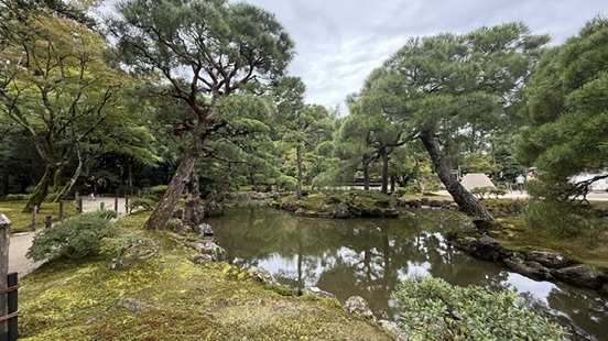 銀閣寺觀音殿深色木造二層建築，白牆黑瓦，周圍是水池與松樹