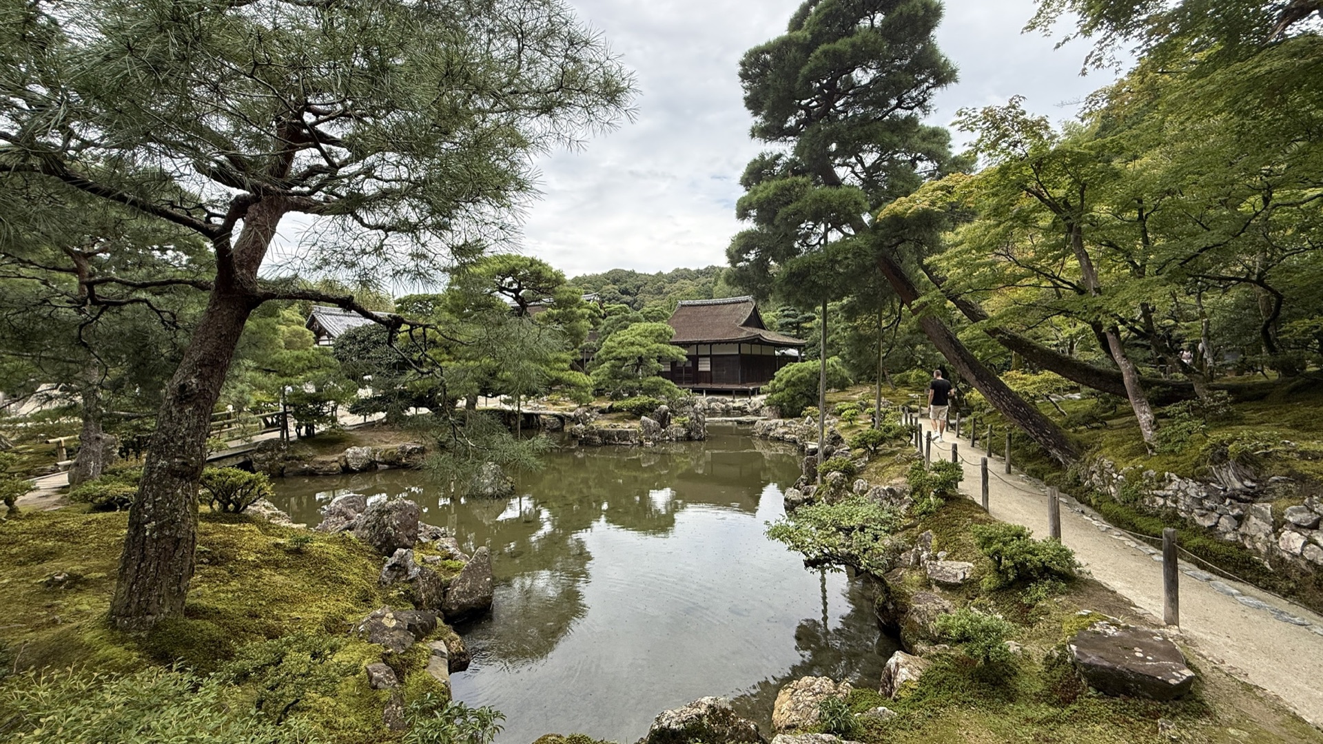 銀閣寺觀音殿深色木造二層建築，白牆黑瓦，周圍是水池與松樹