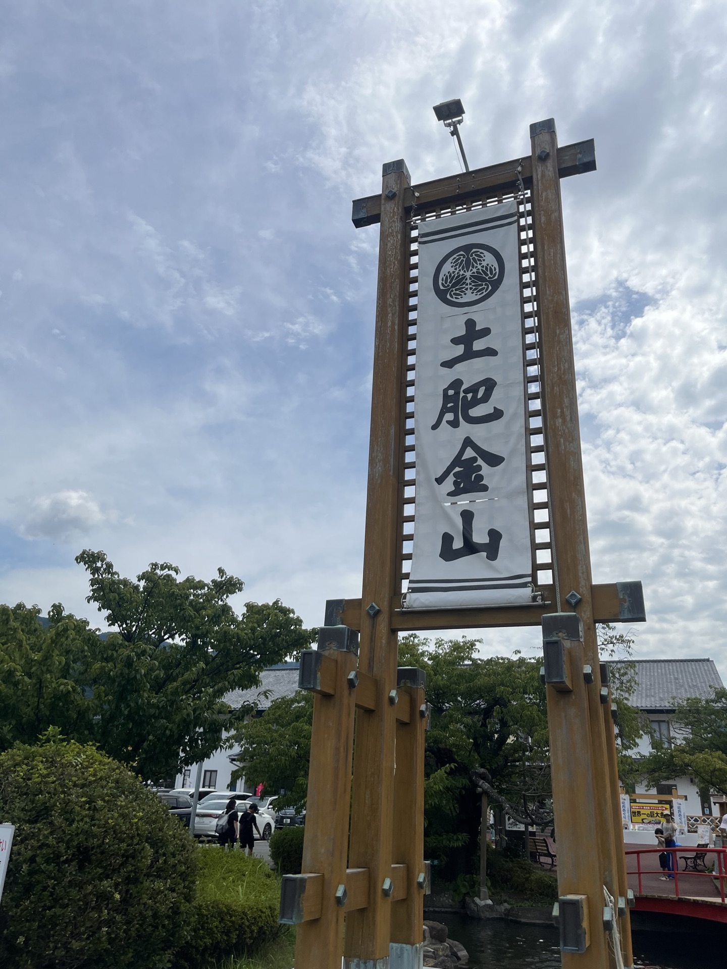 土肥金山入口木製招牌，白色布幔上寫「土肥金山」三字，背景為晴天