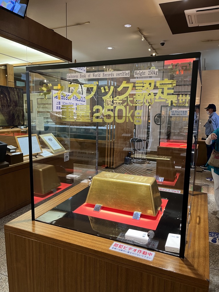 土肥金山入口木製招牌，白色布幔上寫「土肥金山」三字，背景為晴天